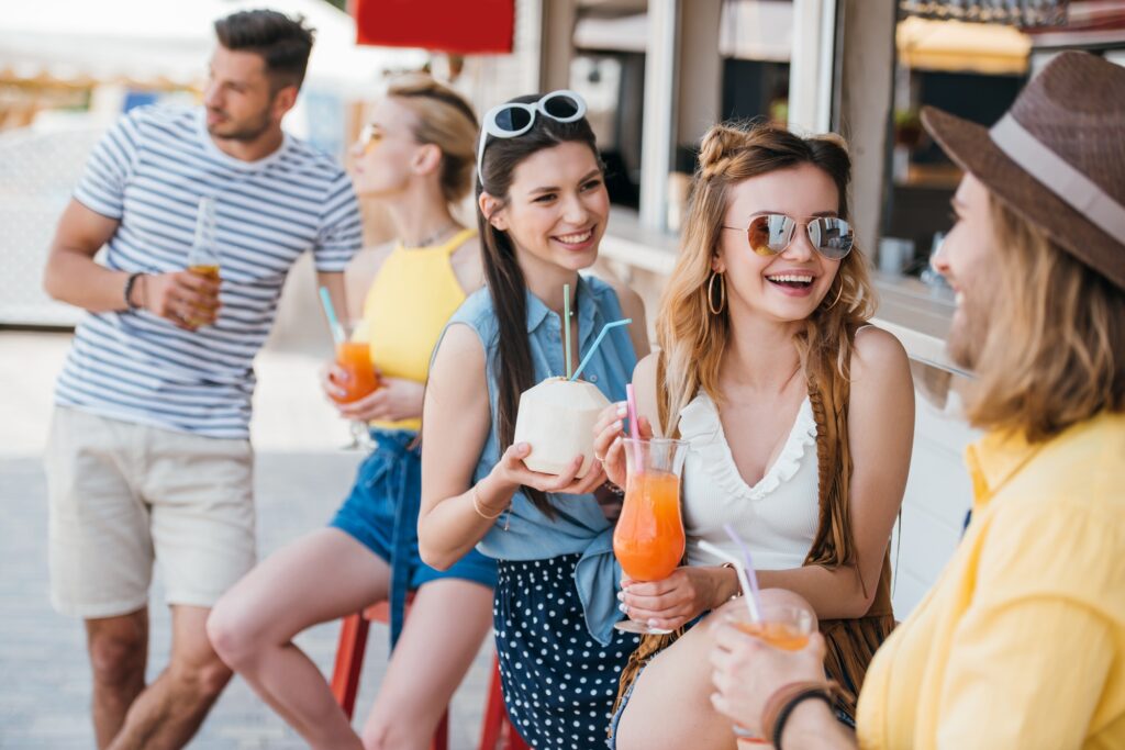 happy young men and women drinking summer cocktails at beach bar